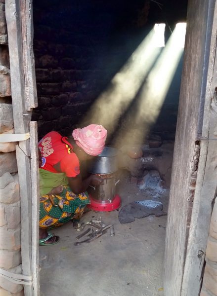 A woman in rural Malawi starts a gasifier stove inside her home.